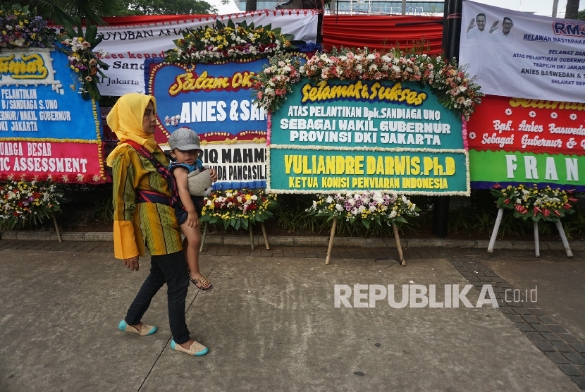 Warga melintas disamping karangan bunga yang berisi ucapan selamat kepada Anies Baswedan dan Sandiaga Uno di Balai Kota DKI Jakarta, Senin (16/10).