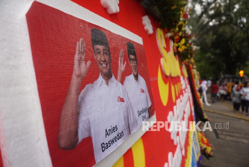 Warga melintas disamping karangan bunga yang berisi ucapan selamat kepada Anies Baswedan dan Sandiaga Uno di Balai Kota DKI Jakarta, Senin (16/10).