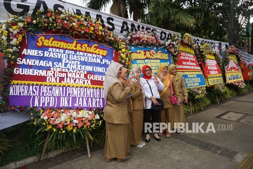 Warga melintas disamping karangan bunga yang berisi ucapan selamat kepada Anies Baswedan dan Sandiaga Uno di Balai Kota DKI Jakarta, Senin (16/10). 
