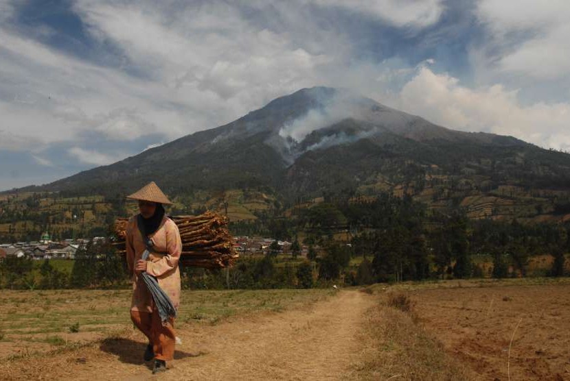 Warga melintasi areal ladang dengan latar belakang kebakaran hutan Gunung Sumbing di Desa Kledung, Temanggung, Jawa Tengah, Minggu (16/9).