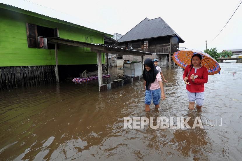 Warga melintasi banjir yang menggenangi kawasan permukiman mereka (ilustrasi) 