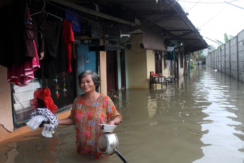 Warga melintasi banjir yang merendam kawasan permukiman Kampung Buaran, Harapan Mulya, Bekasi, Jawa Barat, Minggu (19/2). 