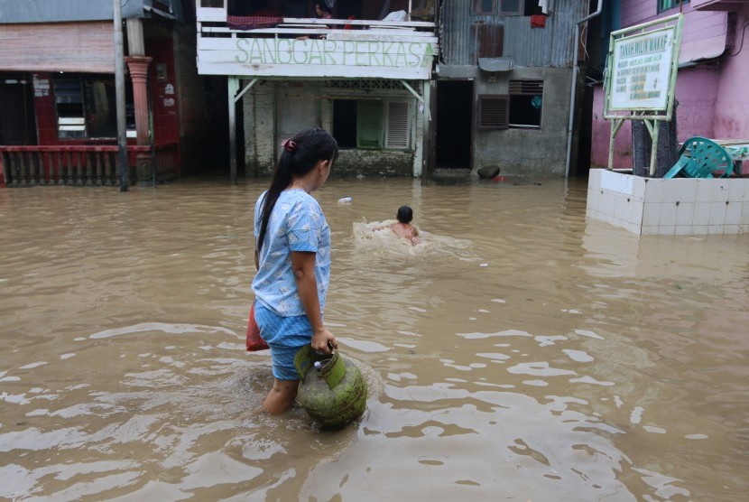 Warga melintasi banjir yang merendam permukiman penduduk, di kawasan pinggir Sungai Deli, di Medan, Sumatera Utara, Rabu (27/9). 
