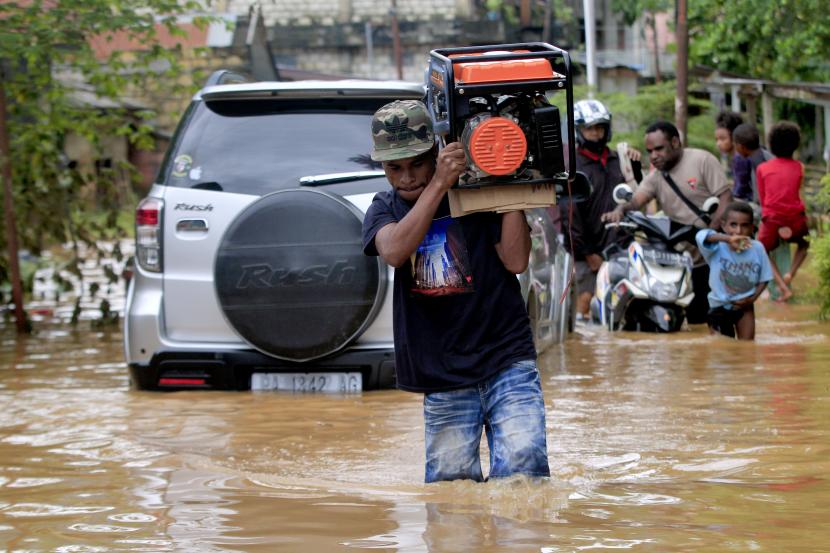 Warga melintasi daerah yang masih terendam banjir di Perumahan Organda, Distrik Heram, Kota Jayapura, Papua, Ahad (9/1/2022). Sekitar tujuh ribu warga terdampak banjir dan longsor yang terjadi pada Jumat (7/1/2022).