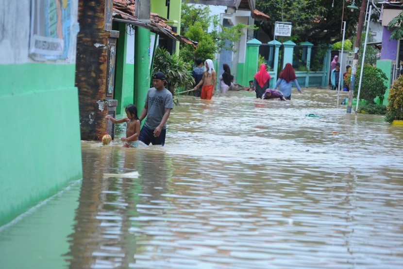 Warga melintasi gang yang digenangi banjir di kabupaten Sampang, Jawa Timur. PLN memadamkan aliran listrik di Sampang, Madura, Jatim karena tingginya banjir.
