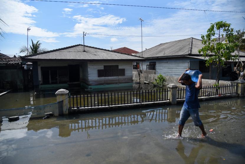 Warga melintasi genangan air akibat banjir rob di kawasan nelayan bagan deli, Belawan, Kota Medan, Sumatera Utara.