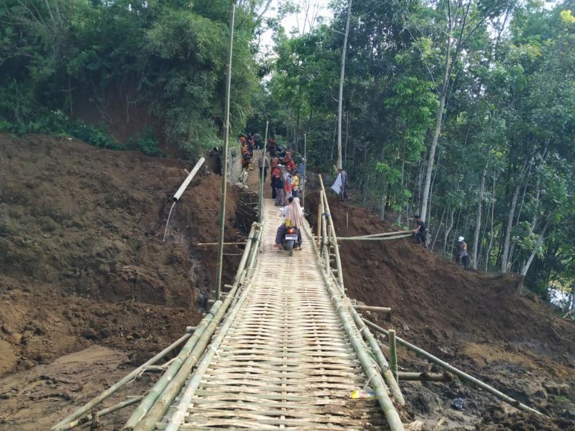 Warga melintasi jembatan darurat yang dibangun pascalongsor di Kampung Bugel, Desa Bugel, Kecamatan Ciawi, Kabupaten Tasikmalaya, Jumat (12/6). .