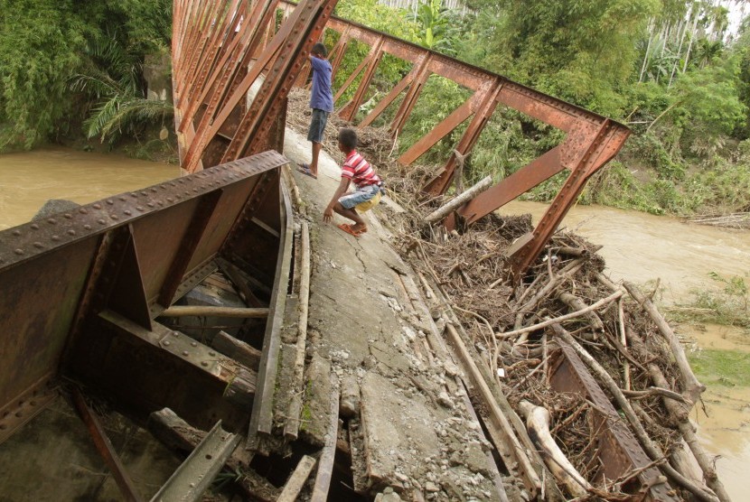 Warga melintasi jembatan yang rusak pascabanjir luapan Sungai Bugha di Desa Bugha, Kecamatan Seulimum, Kabupaten Aceh Besar, Aceh, Senin (2/1). 
