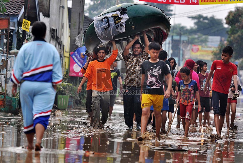 Warga melintasi lupur sisa banjir di Perumahan Pondok Gede Permai, Bekasi, Ahad (23/2). 