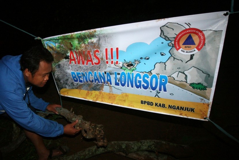 Warga membantu memasang tanda bahaya di sekitar daerah longsor Dusun Dlopo, Desa Kepel, Kecamatan Ngetos, Nganjuk, Jawa Timur, Minggu (9/4).