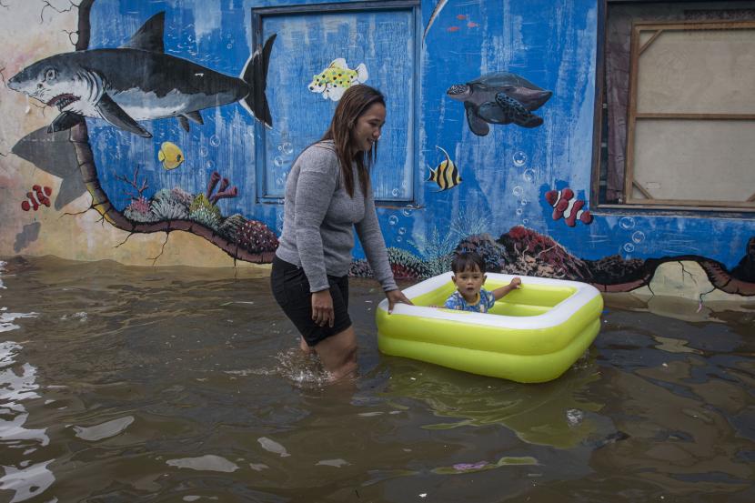 Warga membawa anaknya melintasi banjir pasang air laut atau rob di Kampung Japat, Ancol, Pademangan, Jakarta, Sabtu (4/12).