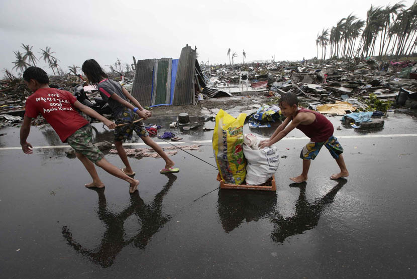   Warga membawa barang-barang bantuan melewati rumah yang hancur di kota Tacloban, Leyte provinsi Leyte, Filipina tengah, Ahad (10/11).  (AP/Bullit Marquez)