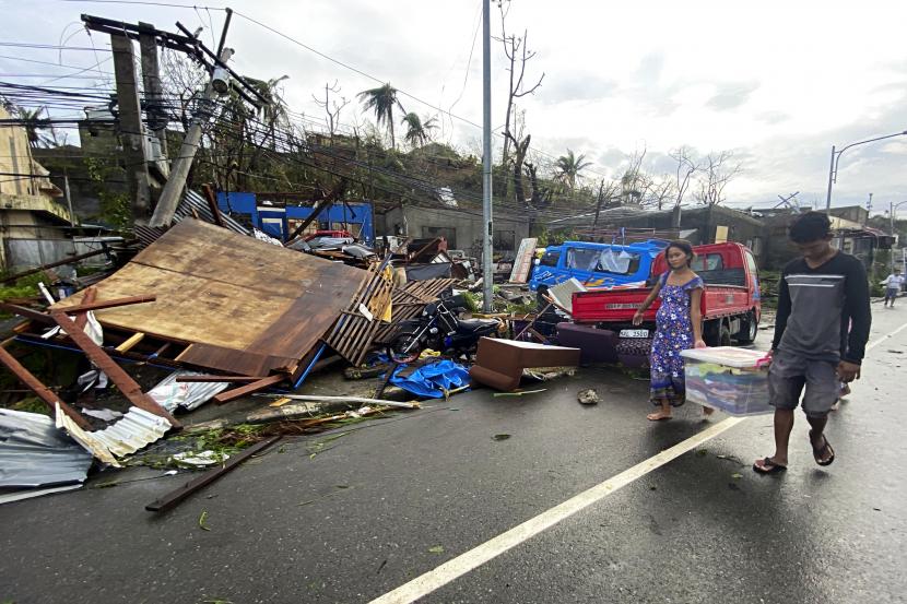 Warga membawa barang-barang yang tersisa saat berjalan melewati rumah yang rusak akibat Topan Rai di kota Surigao, Surigao del Norte, Filipina tengah, Jumat 17 Desember 2021. Penduduk di daerah-daerah yang terkena dampak Topan Rai memohon bantuan.