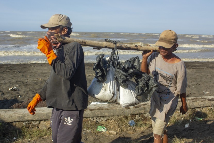Warga membawa karung berisi pasir yang tercemar tumpahan minyak mentah (Oil Spill) di pesisir Pantai Cemarajaya, Karawang, Jawa Barat, Rabu (24/7/2019).