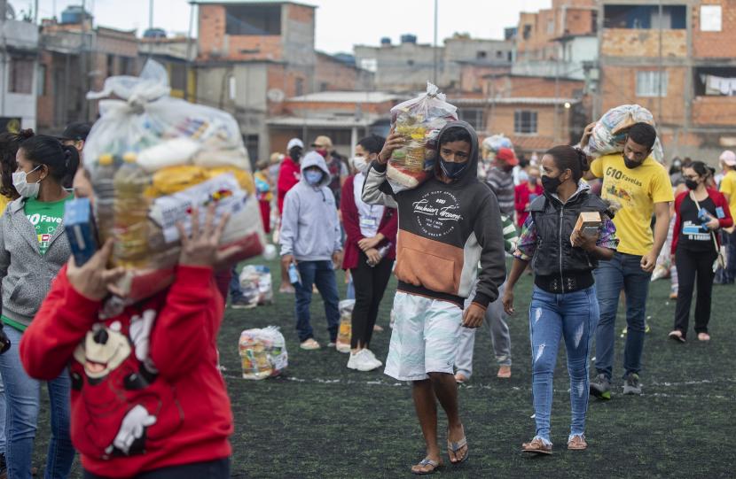Warga membawa tas makanan sumbangan LSM lokal G10 Favelas yang dibagikan di lapangan sepak bola di tengah pandemi COVID-19 di kawasan Capao Redondo, Sao Paulo, Brasil, Senin 26 April 2021.