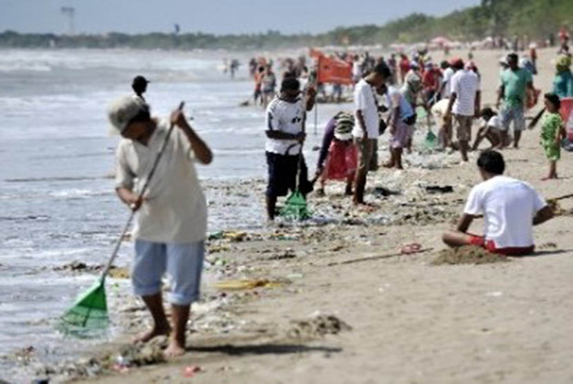 Warga membersihkan sampah yang terdampar dan mengganggu wisatawan di Pantai Kuta, Bali.