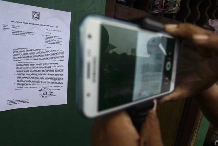 Warga memotret menggunakan telepon seluler surat pemberitahuan dari Pemprov DKI Jakarta yang tertempel di salah satu rumah di kawasan Kalijodo, Jakarta, Ahad (14/2). 