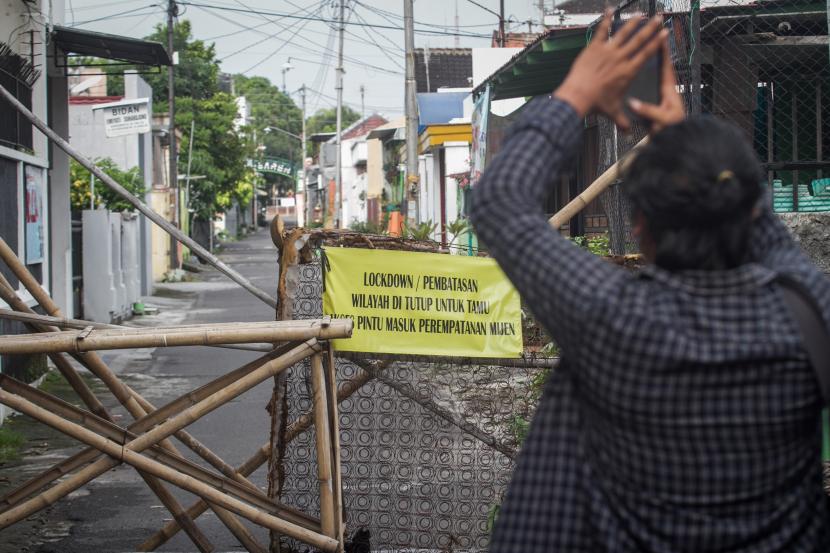 Warga memotret papan pemberitahuan karatina wilayah di Kampung Wonosaren RW VIII, Jagalan, Solo, Jawa Tengah. Beberapa hari terakhir jumlah kematian harian di Solo akibat Covid-19 memang cukup tinggi.