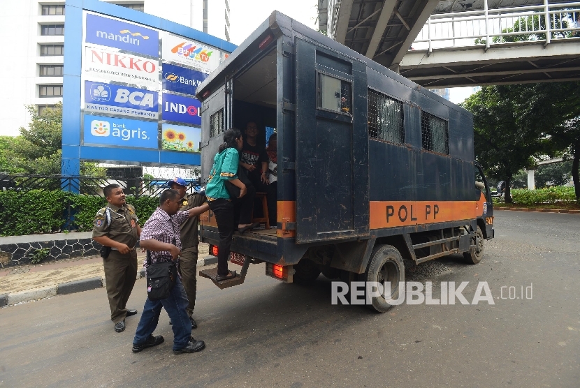 Warga menaiki mobil Satpol PP di Jalan Sudirman, Jakarta Pusat, Selasa (22/3).