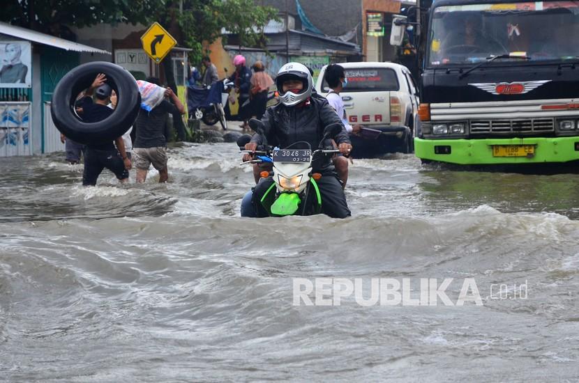 Warga menaiki sepeda motor menerobos banjir yang menggenangi jalan di Desa Tanjung Karang, Jati, Kudus, Jawa Tengah, Senin (8/2/2021). Banjir setinggi 60 cm yang merendam jalan provinsi penghubung kabupaten Kudus-Purwodadi sejak Kamis (4/2/2021) tersebut menyebabkan kemacetan dan puluhan sepeda motor mogok.