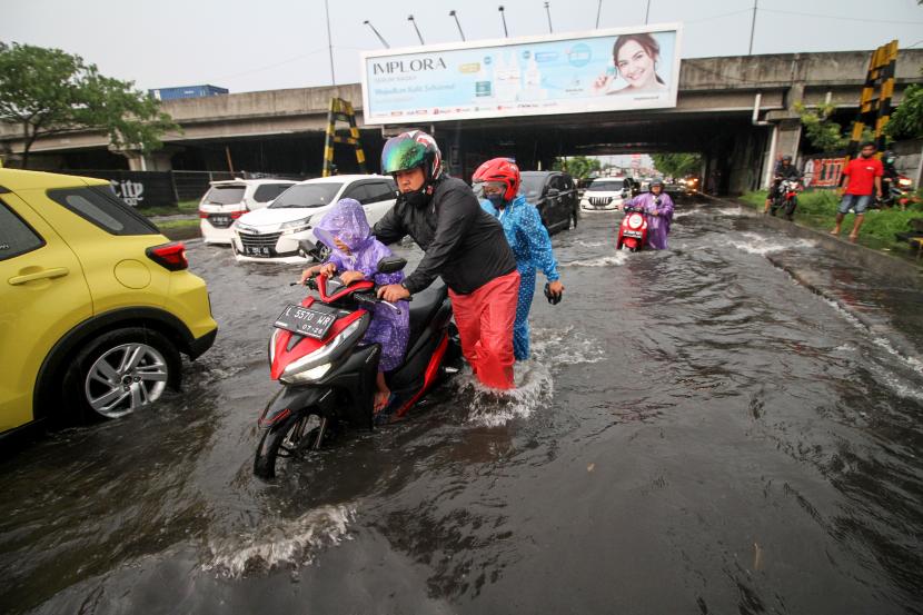 Warga mendorong kendaraannya yang mogok saat melewati banjir di kawasan Jalan Raya Jati, Sidoarjo, Jawa Timur, Ahad (23/10/2022). 