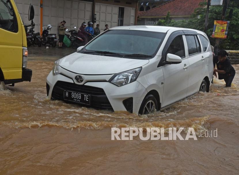Warga mendorong mobil yang mogok saat melintasi genangan banjir, ilustrasi. Badan Nasional Penanggulangan Bencana (BNPB) memantau banjir yang mengenangi 169 rumah warga di Kabupaten Serang, Provinsi Banten, pada Selasa (31/5/2022). 