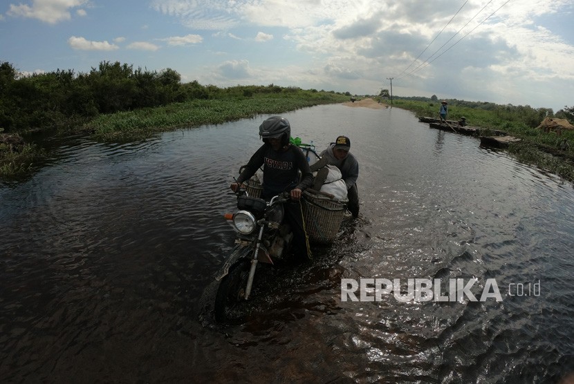Warga mendorong motor yang mogok saat lewati jalan penghubung Desa Jebus dengan Desa Gedong Karya yang terendam banjir luapan Sungai Batanghari di Muarojambi, Jambi, Selasa (7/1/2020). 