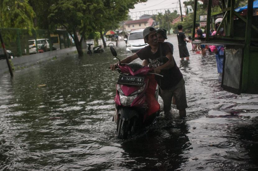 Warga mendorong motornya yang mogok setelah melintasi banjir di Rangkasbitung, Lebak, Banten.