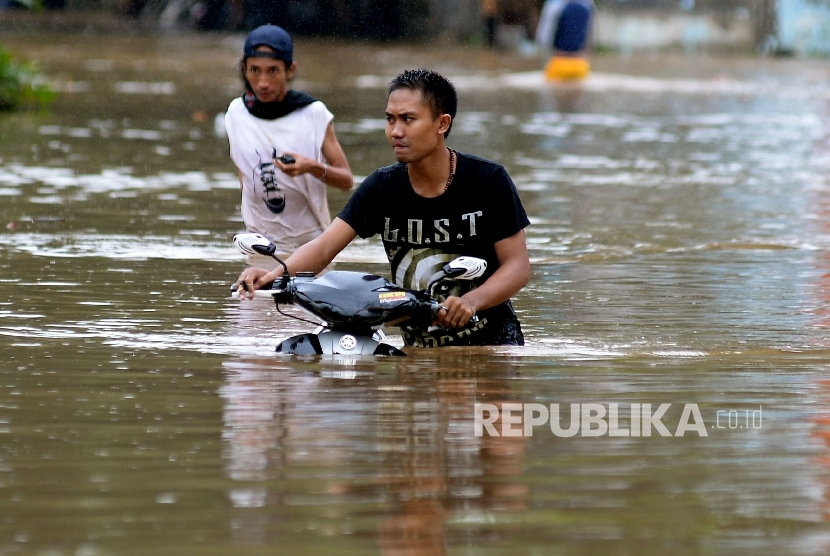 Warga mendorong sepeda motor melintasi banjir akibat air luapan Sungai Ciliwung, Bukit Duri, Jakarta, Kamis (16/2). 