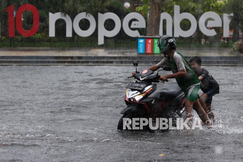 Warga mendorong sepeda motornya yang mogok akibat menerobos banjir di Jalan Tambaksari, Surabaya, Jawa Timur, Sabtu (13/3/2021). Hujan deras yang mengguyur sejumlah kawasan di Surabaya selama dua jam mengakibatkan sejumlah ruas jalan terendam banjir. 