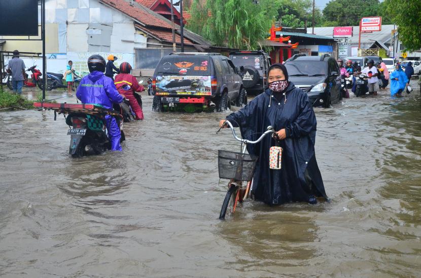 Warga mendorong sepedanya saat melintasi jalan yang tergenang banjir di Desa Tanjung Karang, Jati, Kudus, Jawa Tengah, Jumat (5/2/2021). Banjir yang merendam jalan provinsi penghubung kabupaten Kudus-Purwodadi setinggi 50 cm sejak Kamis (4/2/2021) tersebut terjadi akibat tingginya intensitas hujan.