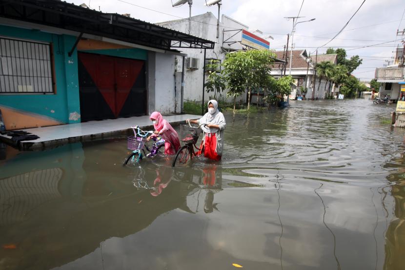 Warga mendorong sepedanya saat menerobos banjir di kawasan Waru, Sidoarjo, Jawa Timur. 