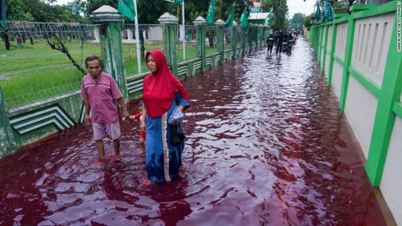 Warga mengarungi air banjir yang diwarnai merah dari limbah pabrik batik di Pekalongan, Jawa Tengah pada 6 Februari.