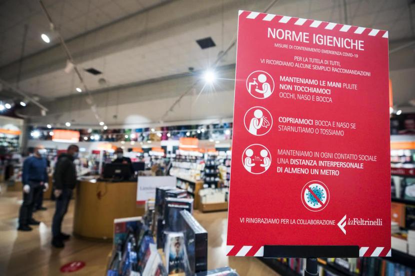 Warga mengenakan masker dalam toko buku di Roma, Italia, Senin (20/4). Italia mencatat angka kematian harian terendah terkait corona pada Ahad. Prancis dan Spanyol juga demikian. 