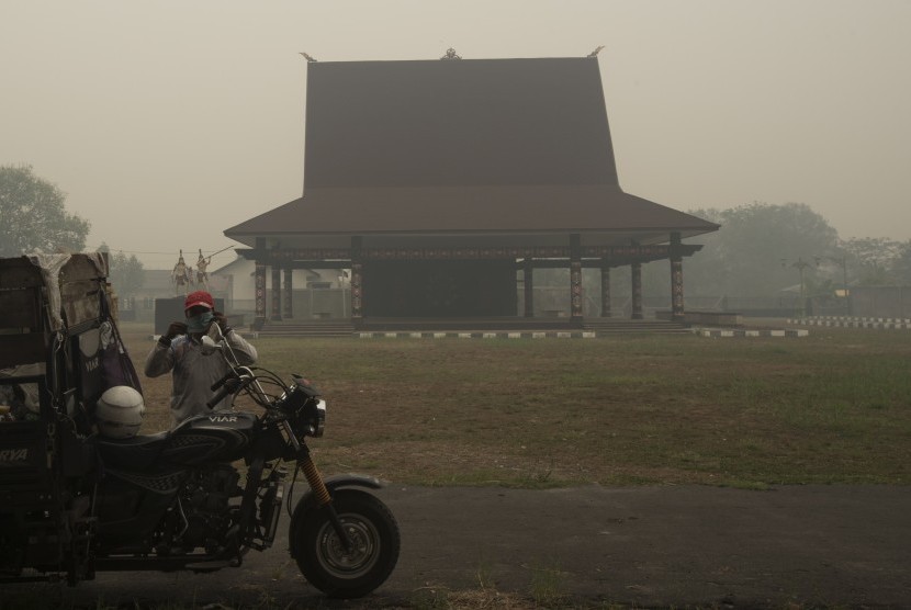 Warga mengenakan masker dengan latar bangunan panggung dayak yang masih diselimuti asap di Palangkaraya, Kalimantan Tengah, Kamis (1/10). 