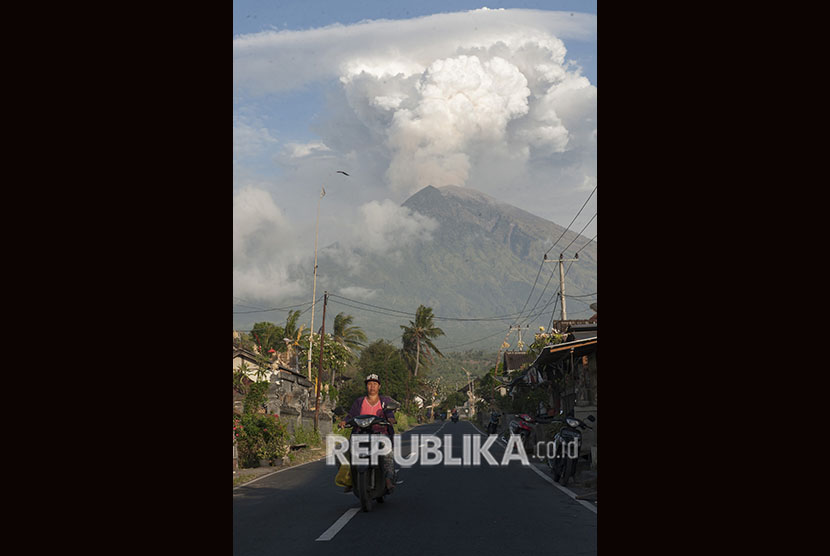 Warga mengendarai sepeda motor dengan latar belakang erupsi Gunung Agung di Desa Culik, Karangasem, Bali, Jumat (29/6).