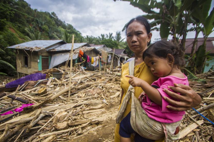 Warga menggendong anaknya berada di dekat puing-puing rumah dan batang pohon yang terbawa arus akibat banjir bandang di Desa Arangani, Kabupaten Hulu Sungai Tengah, Kalimantan Selatan, Jumat (22/1/2021). Berdasarkan data terakhir dari Badan Penanggulangan Bencana Daerah (BPBD) Provinsi Kalimantan Selatan pada Jumat (22/1/2021) , sebanyak 148.031 KK dengan 505.557 jiwa terdampak bencana banjir di Kalimantan Selatan.