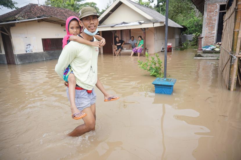 Warga menggendong anaknya melintasi jalan yang terendam banjir di Desa Ngadirenggo, Trenggalek, Jawa Timur, Sabtu (8/10/2022).