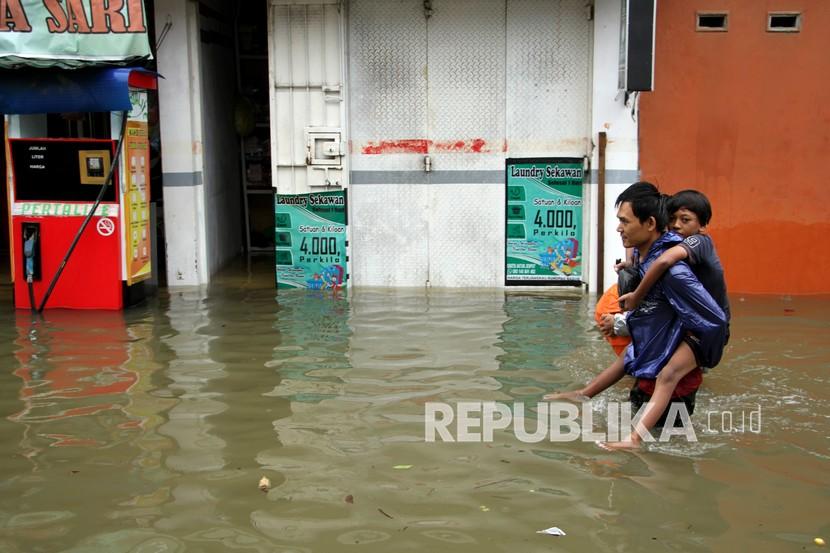 Warga menggendong anaknya saat menerobos banjir. Ratusan rumah di daerah terendam banjir akibat curah hujan yang tinggi dan sebagian warga sudah mulai mengungsi.