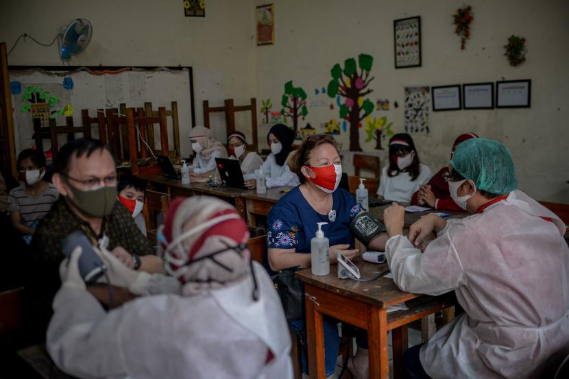 Warga menggunakan masker merah putih memeriksa kesehatan sebelum mendapatkan vaksin Covid-19 di SDN 05 Kembang Sepatu, Kramat, Jakarta.