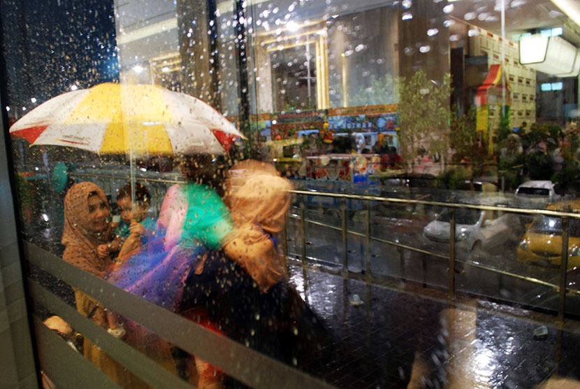 Warga menggunakan payung ketika hujan deras di salah satu pusat perbelanjaan di Pekanbaru, Riau, Selasa (27/10) malam. 