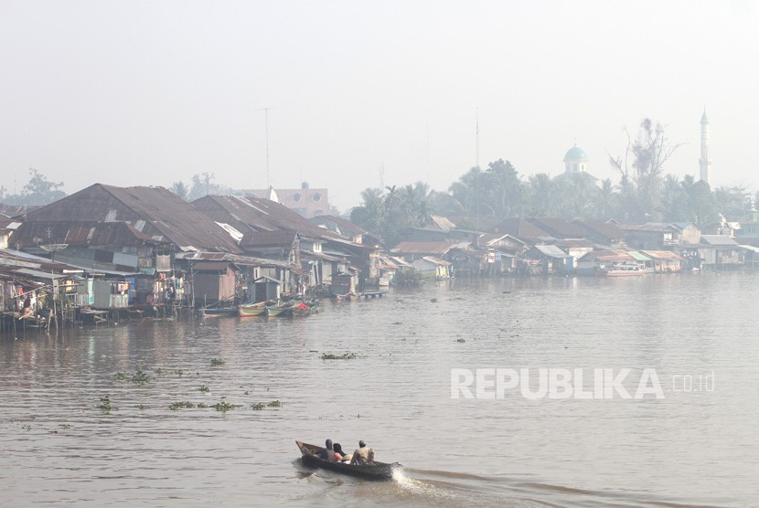 Warga menggunakan perahu bermesin, melintas di Sungai Martapura yang diselimuti kabut asap di Kota Banjarmasin, Kalimantan Selatan, Jumat (8/11/2019). 