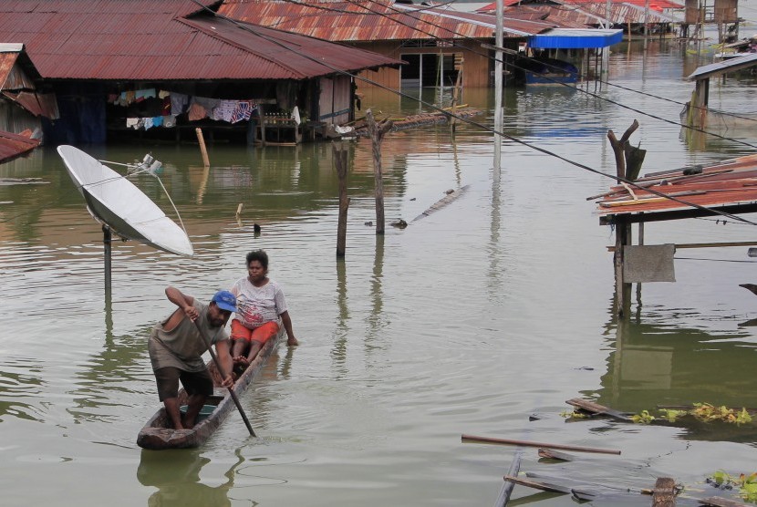 Warga menggunakan perahu melintas di antara rumah yang terendam banjir akibat meluapnya Danau Sentani dampak dari banjir badang Sentani di Kampung Yoboi, Sentani, Jayapura, Papua, Jumat (22/3/2019). 