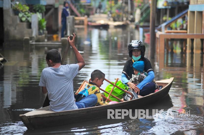 Warga menggunakan perahu melintasi jalan permukiman yang terendam luapan banjir (ilustrasi)
