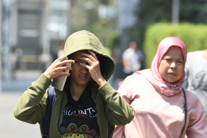 Warga menghalau sinar matahari dengan pakaiannya saat melakukan aktivitas di kawasan Bundaran Hotel Indonesia, Jakarta, Selasa (22/10/2019). 