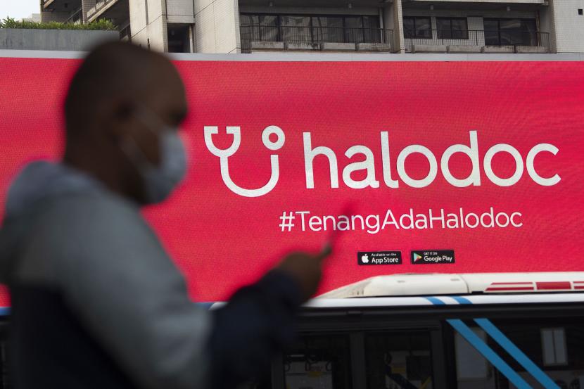 Warga mengoperasikan telepon pintarnya dengan berlatar belakang sebuah reklame produk startup nasional, Halodoc, di Jalan Jenderal Sudirman, Jakarta.