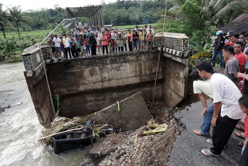 Warga menonton oprit atau sambungan antara jalan dengan jembatan Kali Klawing, yang ambles akibat tergerus aliran air, di Desa Majapura, Bobotsari, Purbalingga, Jateng, Ahad (19/3).