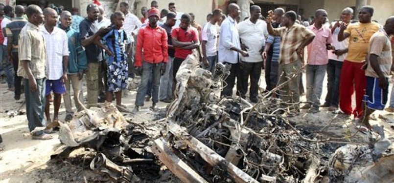 Warga menyaksikan bangkai mobil yang digunakan dalam aksi bom bunuh diri di dekat gereja Katholik St. Theresa di Madalla, Nigeria, Ahad (25/12). 
