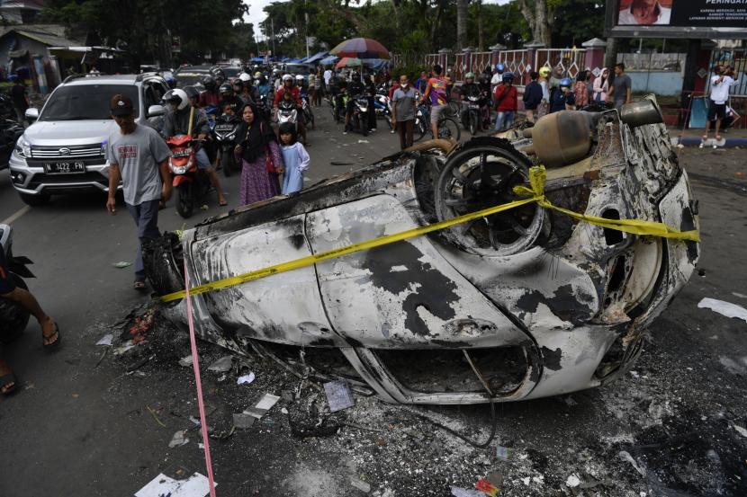 Warga menyaksikan mobil yang hangus terbakar akibat kericuhan usai pertandingan BRI Liga 1 antara Arema melawan Persebaya di Stadion Kanjuruhan, Malang, Jawa Timur, Ahad (2/10/2022). Sedikitnya 129 orang dilaporkan meninggal dunia dan 13 mobil rusak akibat kerusuhan tersebut. 