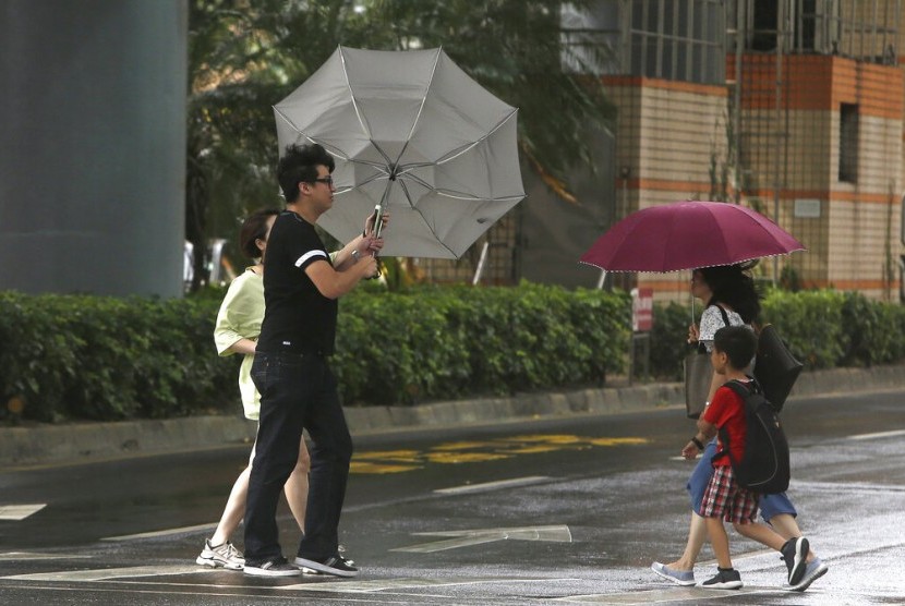 Warga menyeberang jalan di tengah tiupan angin kencang yang disebabkan oleh Topan Bailu di Taipei, Taiwan, Sabtu (24/8).